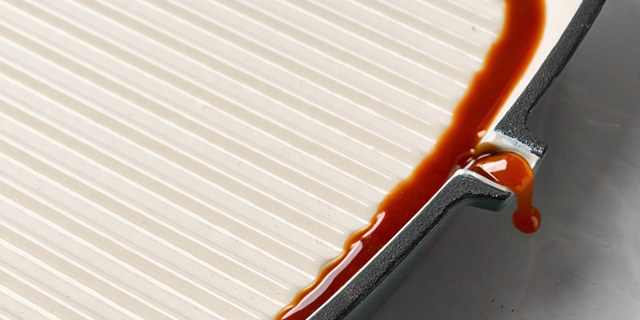 Close-up of ProChef cast iron grill pan interior showing cream enamel ridged surface with sauce dripping from side spout.