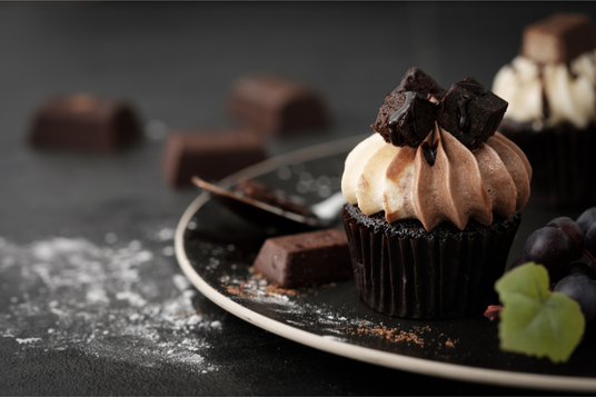 Chocolate cupcake with cream and chocolate pieces on a dark surface