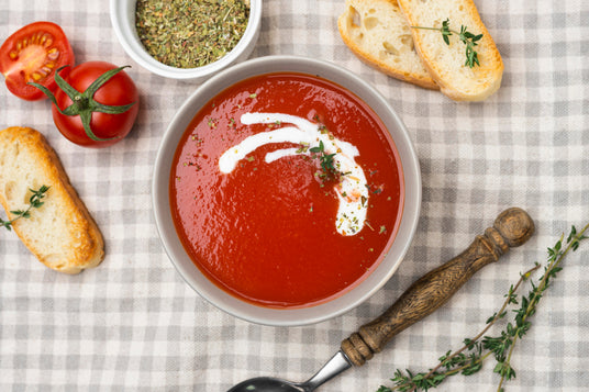 Tomato soup with cream, thyme, and bread on a checkered tablecloth