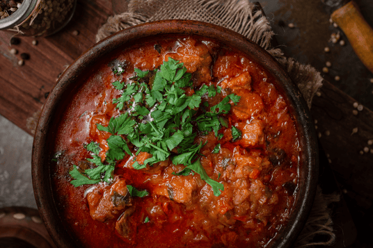 Red stew with herbs in a wooden bowl on a rustic background