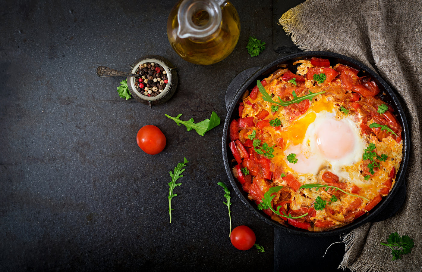 Skillet with Shakshuka on a dark surface with tomatoes and herbs