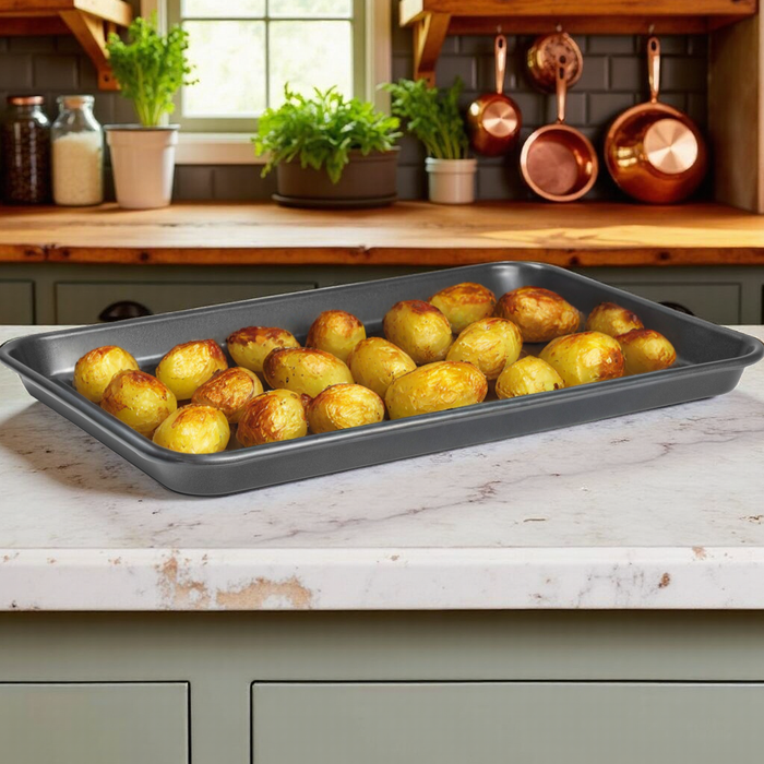 Roasted potatoes on a baking tray in a kitchen setting with copper pots and greenery.