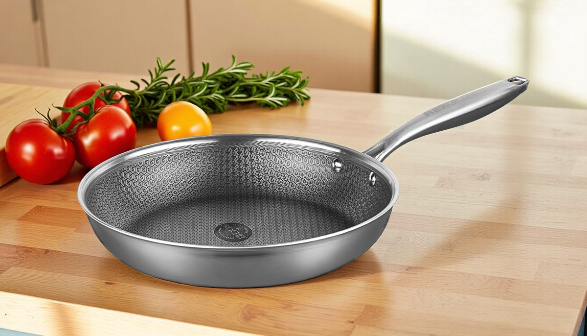 Stainless steel frying pan on a wooden surface with vegetables in the background