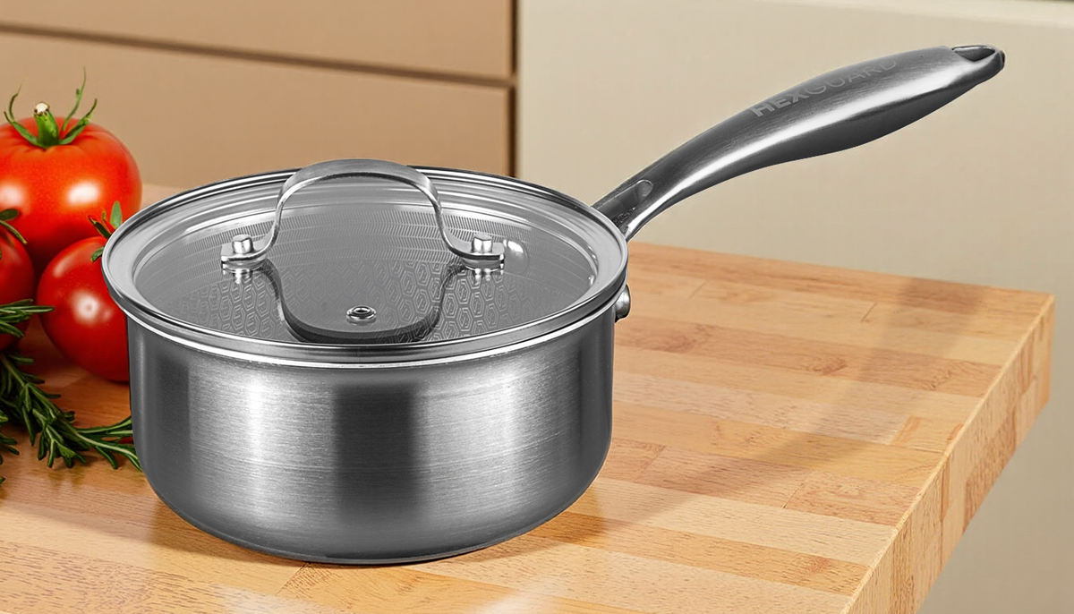 Stainless steel saucepan with lid on a wooden surface with tomatoes and rosemary.