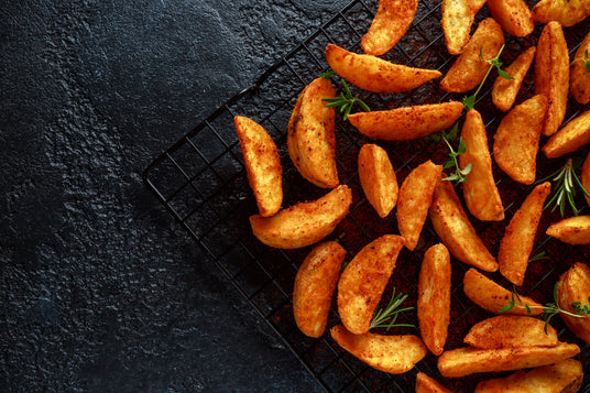 Roasted potato wedges on a cooling rack with rosemary on a dark surface