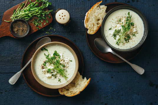 Two bowls of soup with herbs and bread on a dark surface