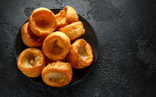 Plate of golden brown Yorkshire puddings on a dark textured surface