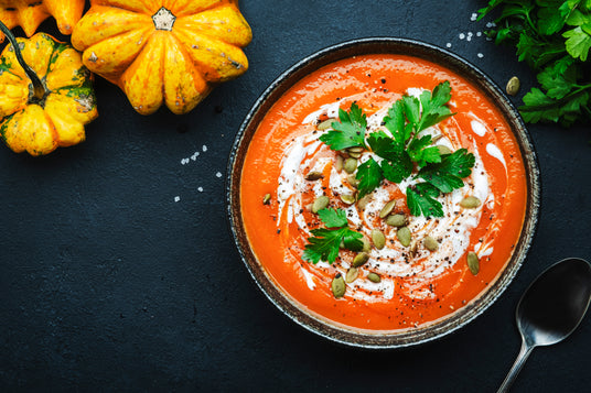  bowl of soup with garnishes on a dark surface with pumpkins