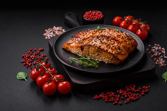Grilled salmon on a black plate with cherry tomatoes and red pepper flakes on a dark surface