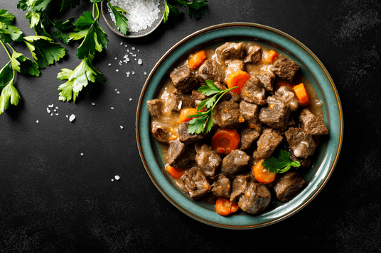Bowl of beef stew with carrots and herbs on a dark surface
