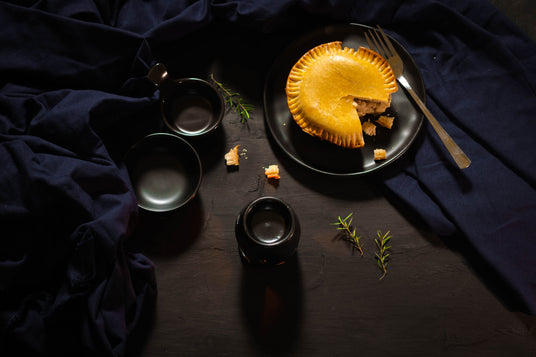 Pie on a dark plate with black bowls and a fork on a dark fabric background