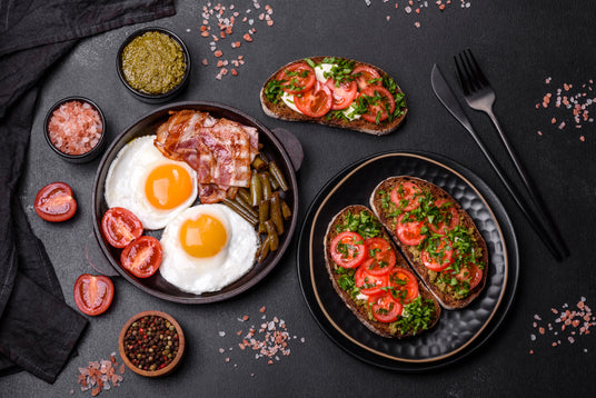 Breakfast spread with eggs, bacon, toast, and vegetables on a dark surface.